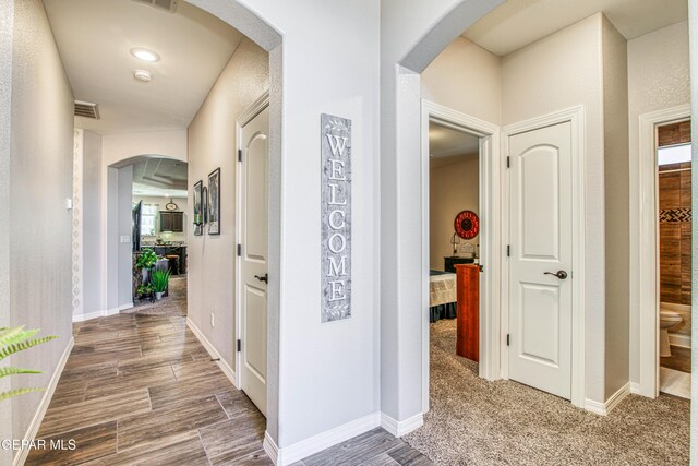 hall featuring arched walkways, baseboards, visible vents, and wood finished floors