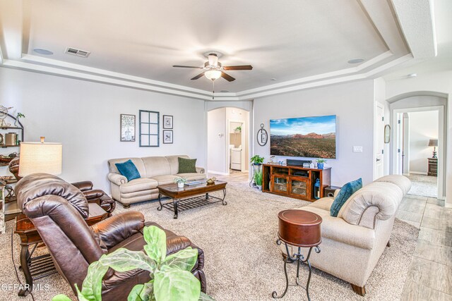 living room featuring visible vents, arched walkways, a ceiling fan, and a tray ceiling