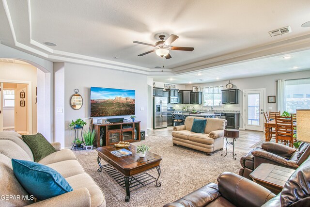 living room with a ceiling fan, visible vents, arched walkways, a tray ceiling, and recessed lighting