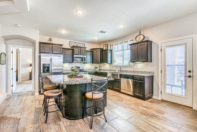 kitchen featuring light stone countertops, dark brown cabinetry, a kitchen breakfast bar, stainless steel appliances, and visible vents
