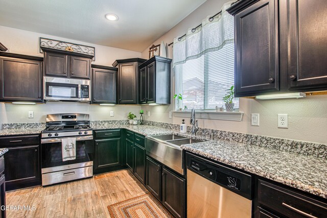 kitchen featuring light stone countertops, recessed lighting, a sink, light wood-style flooring, and appliances with stainless steel finishes