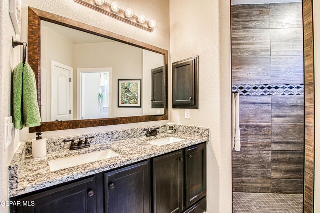 bathroom with double vanity, a textured wall, a tile shower, and a sink