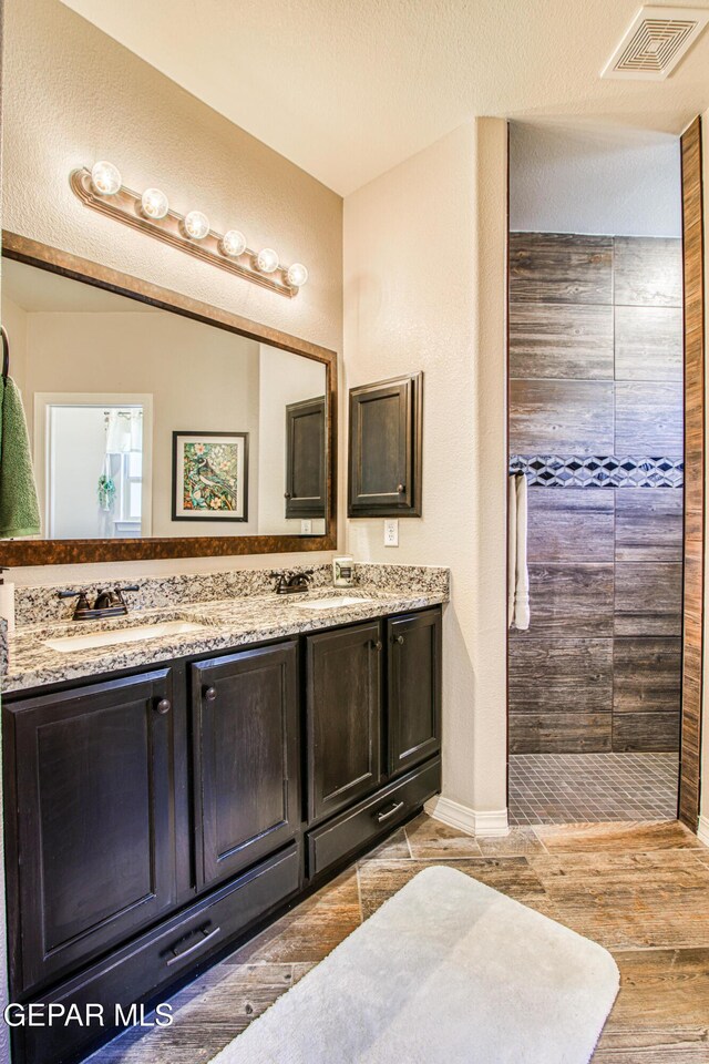 bathroom featuring visible vents, double vanity, wood finished floors, tiled shower, and a sink