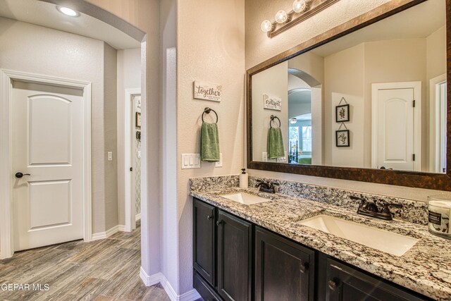 bathroom with double vanity, baseboards, a sink, and wood finished floors