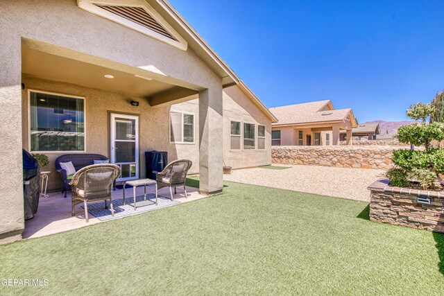back of house featuring a lawn, a patio area, and stucco siding