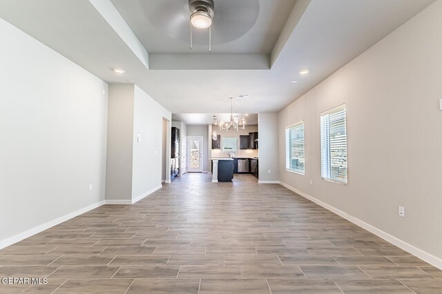 unfurnished living room featuring recessed lighting, baseboards, light wood-style flooring, and ceiling fan with notable chandelier