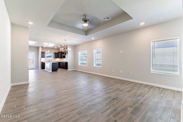 unfurnished living room with visible vents, baseboards, ceiling fan with notable chandelier, and a tray ceiling