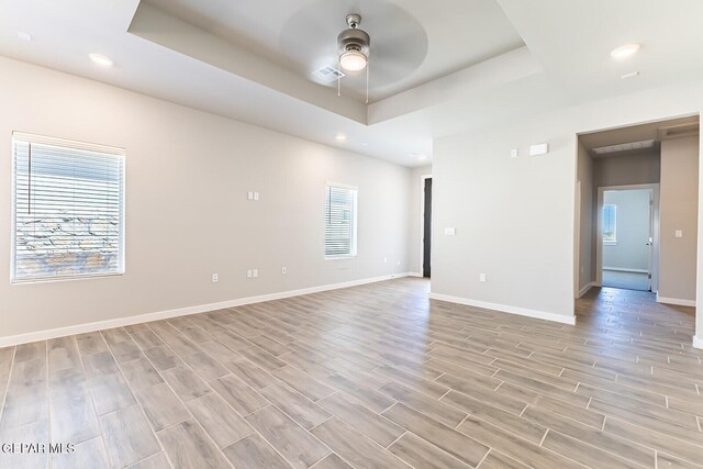 spare room featuring ceiling fan, a raised ceiling, recessed lighting, baseboards, and light wood-type flooring