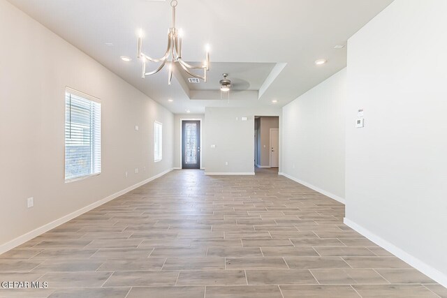 spare room featuring light wood-style floors, baseboards, recessed lighting, a raised ceiling, and ceiling fan with notable chandelier