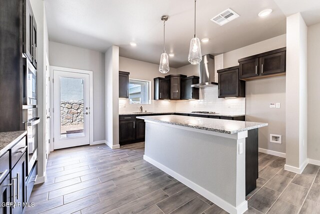 kitchen featuring visible vents, wood finished floors, dark brown cabinetry, wall chimney exhaust hood, and backsplash