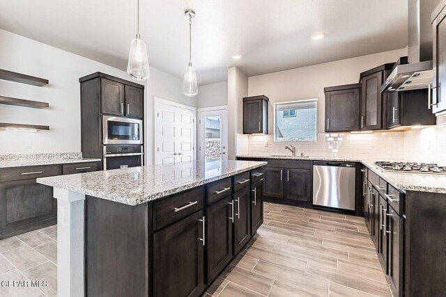 kitchen with a sink, wall chimney exhaust hood, stainless steel appliances, decorative backsplash, and a kitchen island