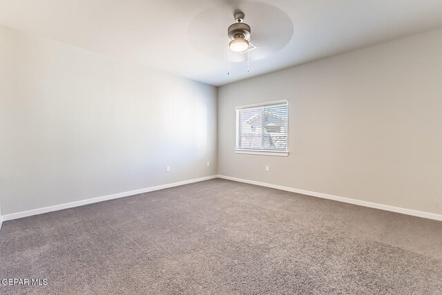 empty room with dark colored carpet, a ceiling fan, and baseboards