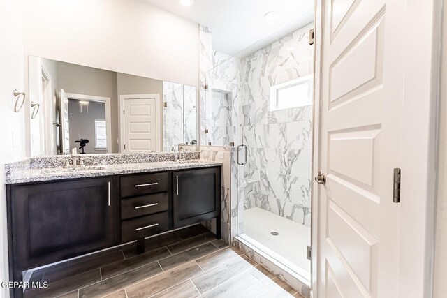 full bath with double vanity, a sink, a marble finish shower, and wood finish floors