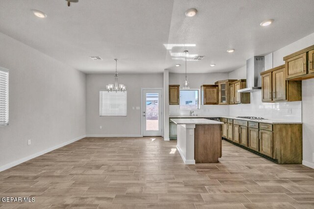 kitchen with brown cabinets, stainless steel gas cooktop, wall chimney exhaust hood, light wood-type flooring, and visible vents