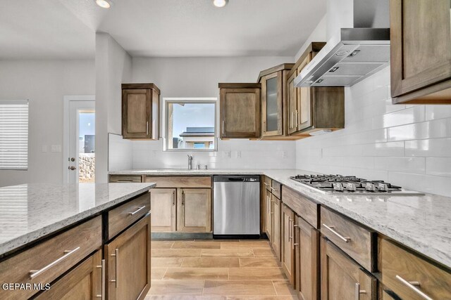 kitchen featuring tasteful backsplash, a sink, light stone counters, stainless steel appliances, and wall chimney exhaust hood