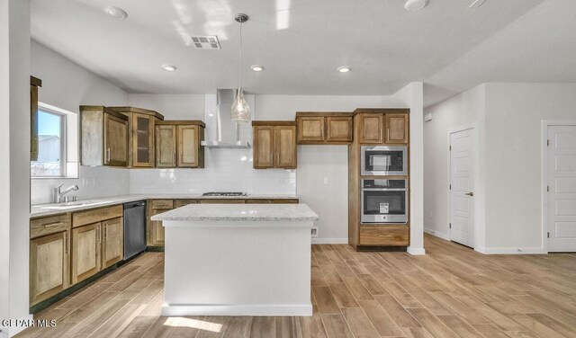 kitchen featuring wall chimney range hood, brown cabinets, a sink, stainless steel appliances, and visible vents