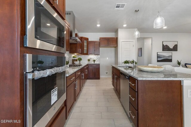 kitchen featuring wall chimney range hood, backsplash, appliances with stainless steel finishes, light stone countertops, and a sink