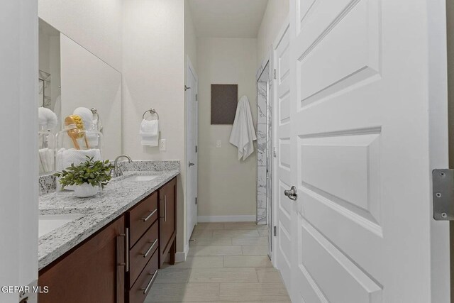 bathroom featuring double vanity, baseboards, a sink, and marble finish floor