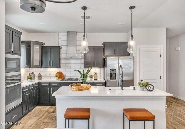 kitchen with a kitchen bar, visible vents, wall chimney exhaust hood, stainless steel appliances, and light wood-style flooring