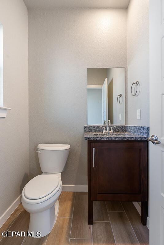half bathroom with toilet, baseboards, wood finished floors, and vanity