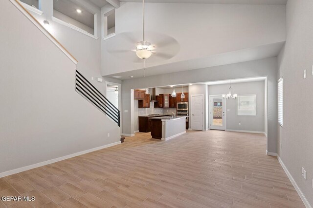 unfurnished living room with stairs, beam ceiling, baseboards, high vaulted ceiling, and ceiling fan with notable chandelier