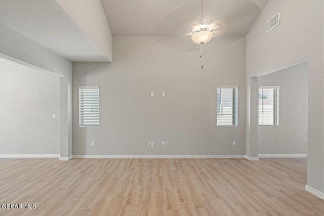 unfurnished room with baseboards, a ceiling fan, light wood finished floors, and a towering ceiling