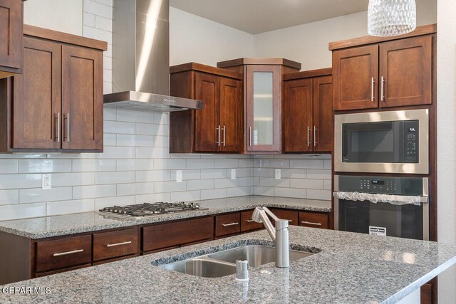 kitchen with a sink, appliances with stainless steel finishes, wall chimney range hood, and tasteful backsplash