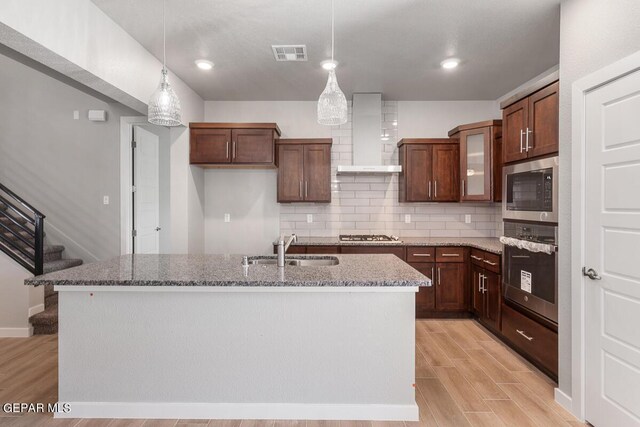 kitchen featuring visible vents, wall chimney exhaust hood, a sink, appliances with stainless steel finishes, and backsplash