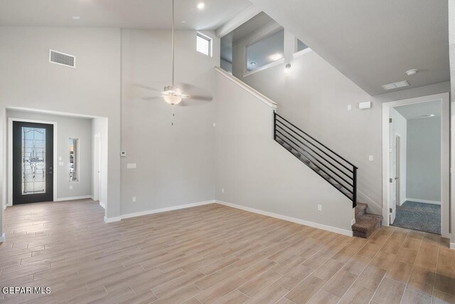 unfurnished living room featuring visible vents, high vaulted ceiling, baseboards, stairs, and light wood-style flooring