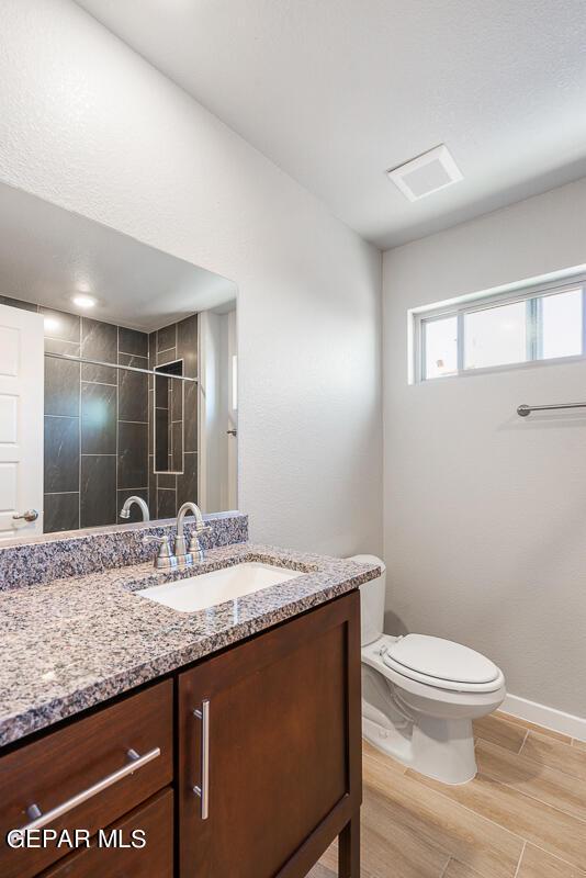 bathroom featuring a tile shower, vanity, toilet, baseboards, and wood finished floors