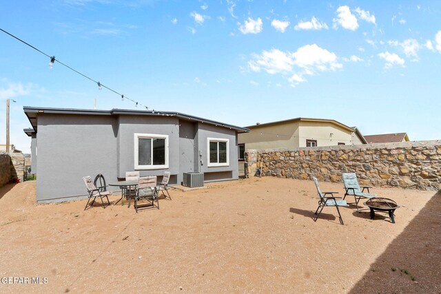 back of house featuring a fenced backyard, central air condition unit, stucco siding, and an outdoor fire pit