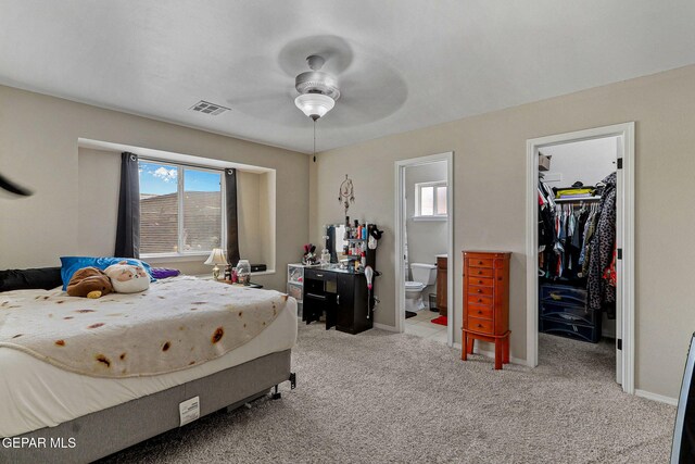 bedroom featuring visible vents, baseboards, light colored carpet, a spacious closet, and ensuite bath