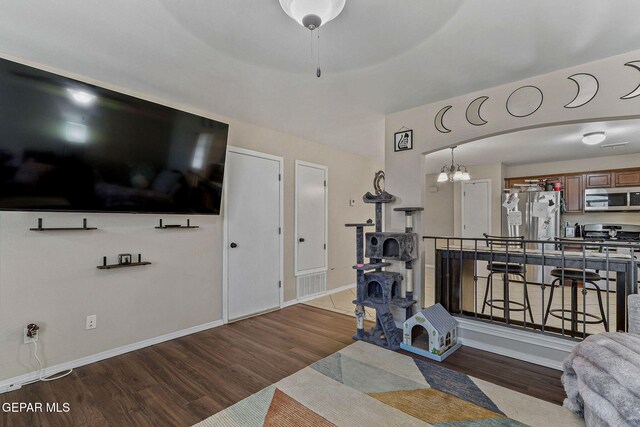 living area with baseboards, arched walkways, wood finished floors, and a notable chandelier