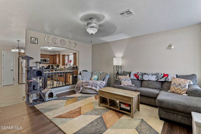 living room featuring a wood stove, ceiling fan with notable chandelier, light wood-type flooring, and visible vents