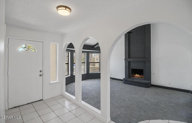foyer entrance featuring a textured ceiling, a fireplace, light tile patterned floors, baseboards, and light carpet