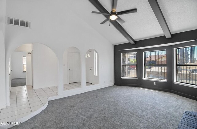 unfurnished living room featuring arched walkways, carpet, beam ceiling, and visible vents