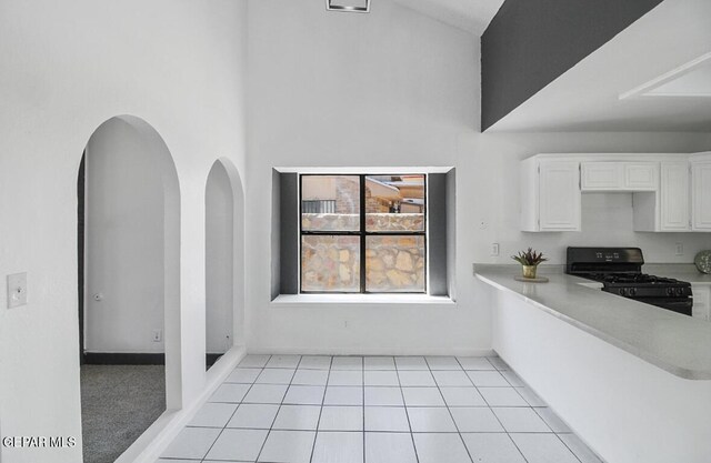 kitchen with black range with gas stovetop, light countertops, arched walkways, white cabinetry, and a towering ceiling