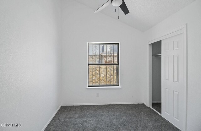 unfurnished bedroom with ceiling fan, dark carpet, baseboards, vaulted ceiling, and a closet