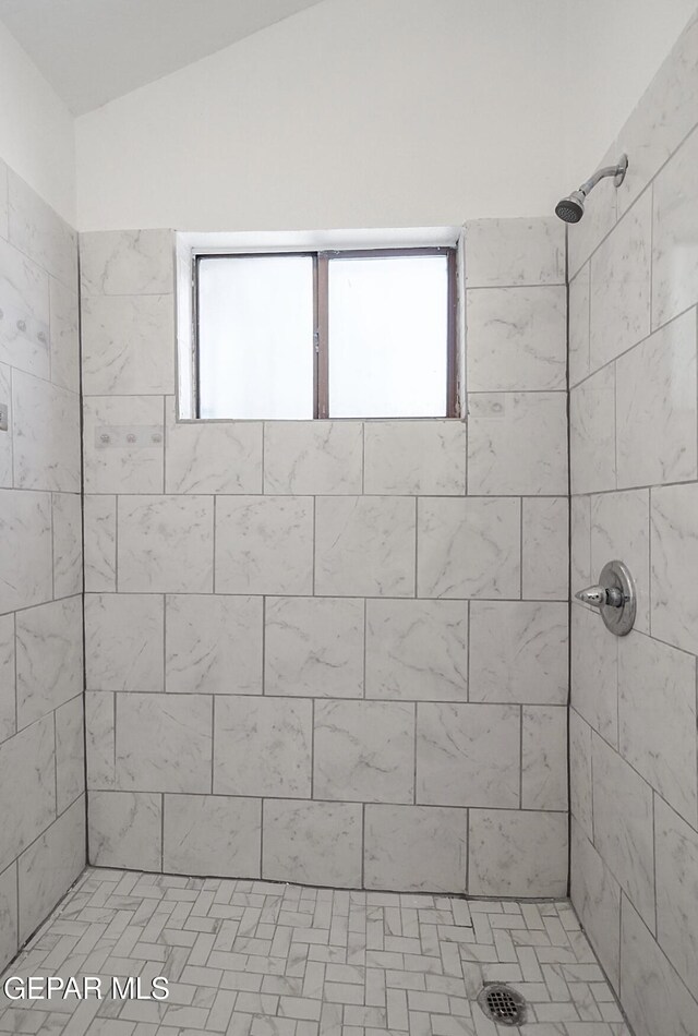 full bath featuring a tile shower and lofted ceiling