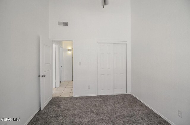 unfurnished bedroom with a towering ceiling, light colored carpet, visible vents, baseboards, and a closet