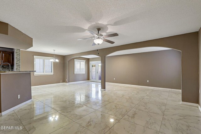 empty room featuring ceiling fan, arched walkways, a textured ceiling, marble finish floor, and baseboards