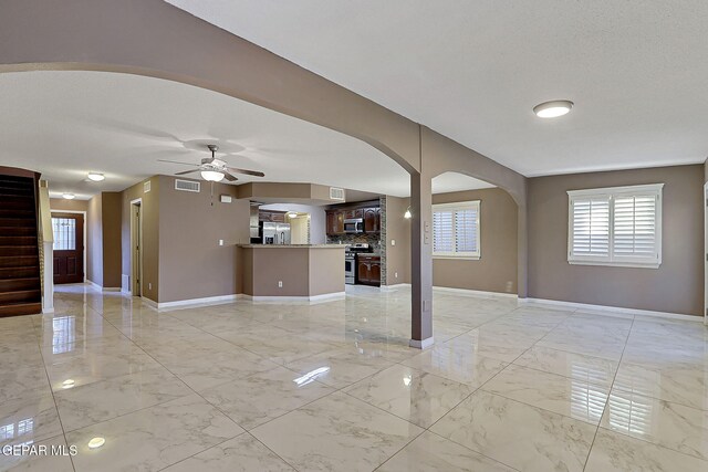 unfurnished living room with arched walkways, baseboards, and marble finish floor