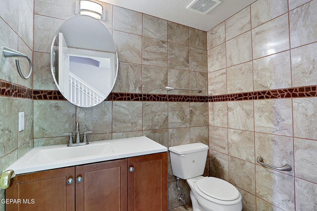 bathroom with visible vents, vanity, toilet, and tile walls
