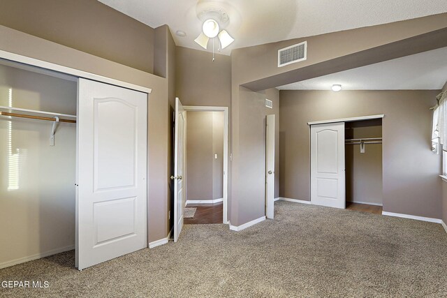 unfurnished bedroom featuring carpet flooring, baseboards, visible vents, and multiple closets