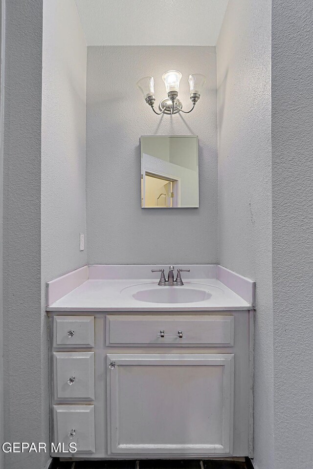 bathroom featuring an inviting chandelier, vanity, and a textured wall