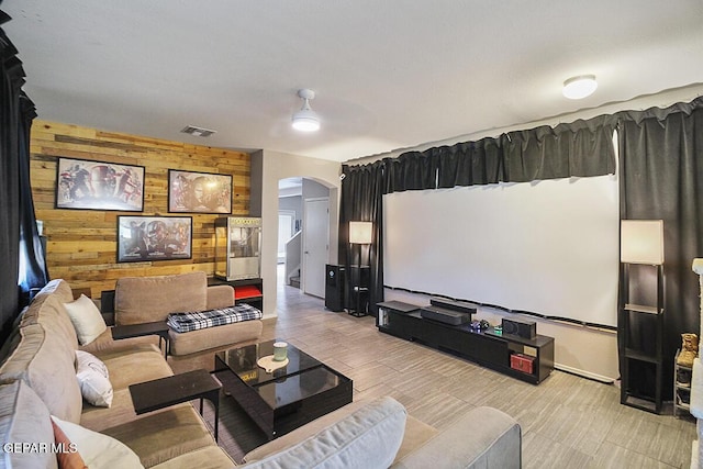 cinema featuring arched walkways, light wood finished floors, wood walls, and visible vents