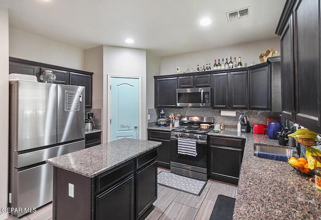 kitchen featuring visible vents, a kitchen island, tasteful backsplash, a sink, and appliances with stainless steel finishes