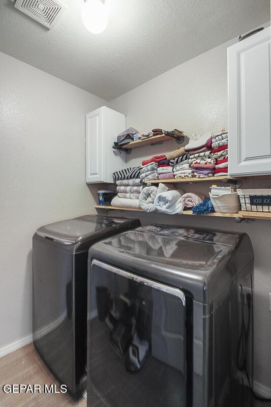 clothes washing area featuring cabinet space, a textured ceiling, baseboards, visible vents, and washer and clothes dryer