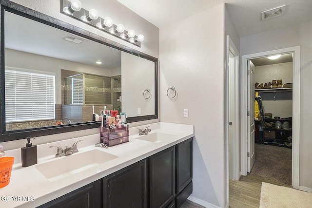 bathroom featuring a sink, a stall shower, double vanity, and visible vents