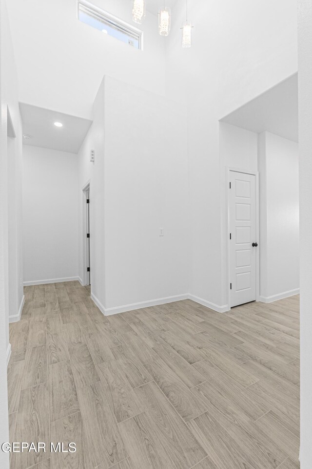 empty room featuring wood finished floors, recessed lighting, baseboards, and a high ceiling